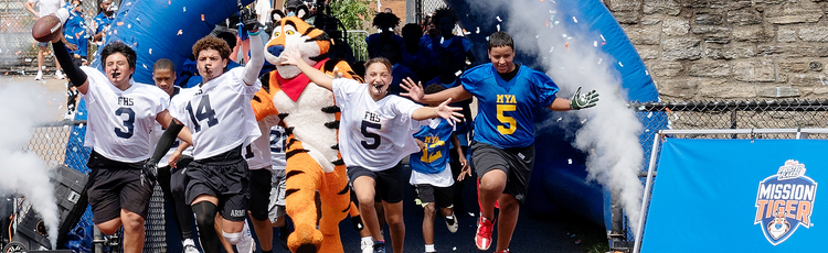 Young athletes running onto a field. Tony the Tiger is with them.