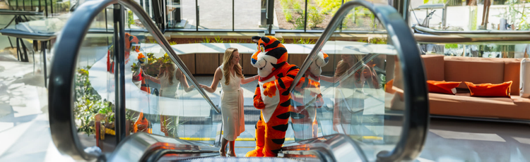 A woman and Tony the Tiger riding up an escalator.