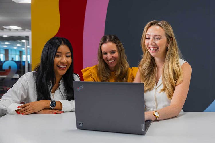 Three employees working on a laptop.
